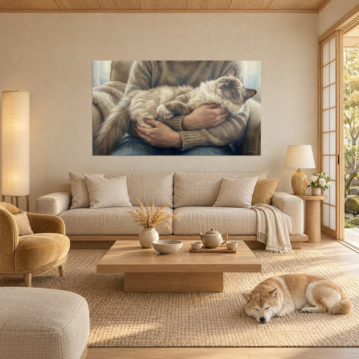 Wall art of a cream ragdoll cat with half-closed eyes, nestled in hands and a beige sweater, above a sofa in a bright living room