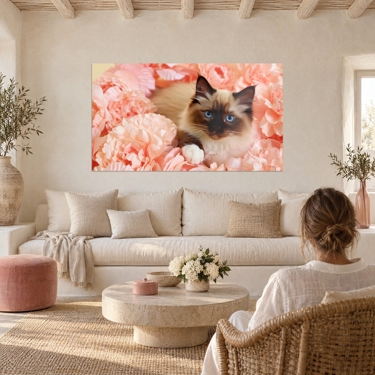 Tableau chaton birman aux yeux bleus lové dans des pivoines roses, pelage crème et brun, au-dessus d'un canapé dans un salon lumineux