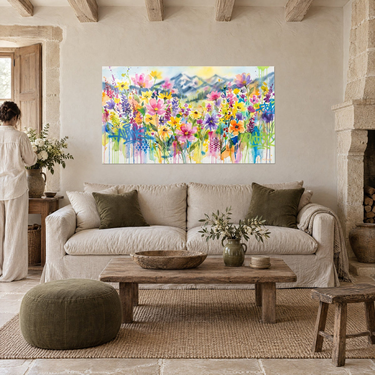 Gemälde Aquarell-Blumenwiese in Rosa und Gelb, bläuliche Berge, türkisfarbene Laufspuren, über einem Sofa in einem hellen Wohnzimmer