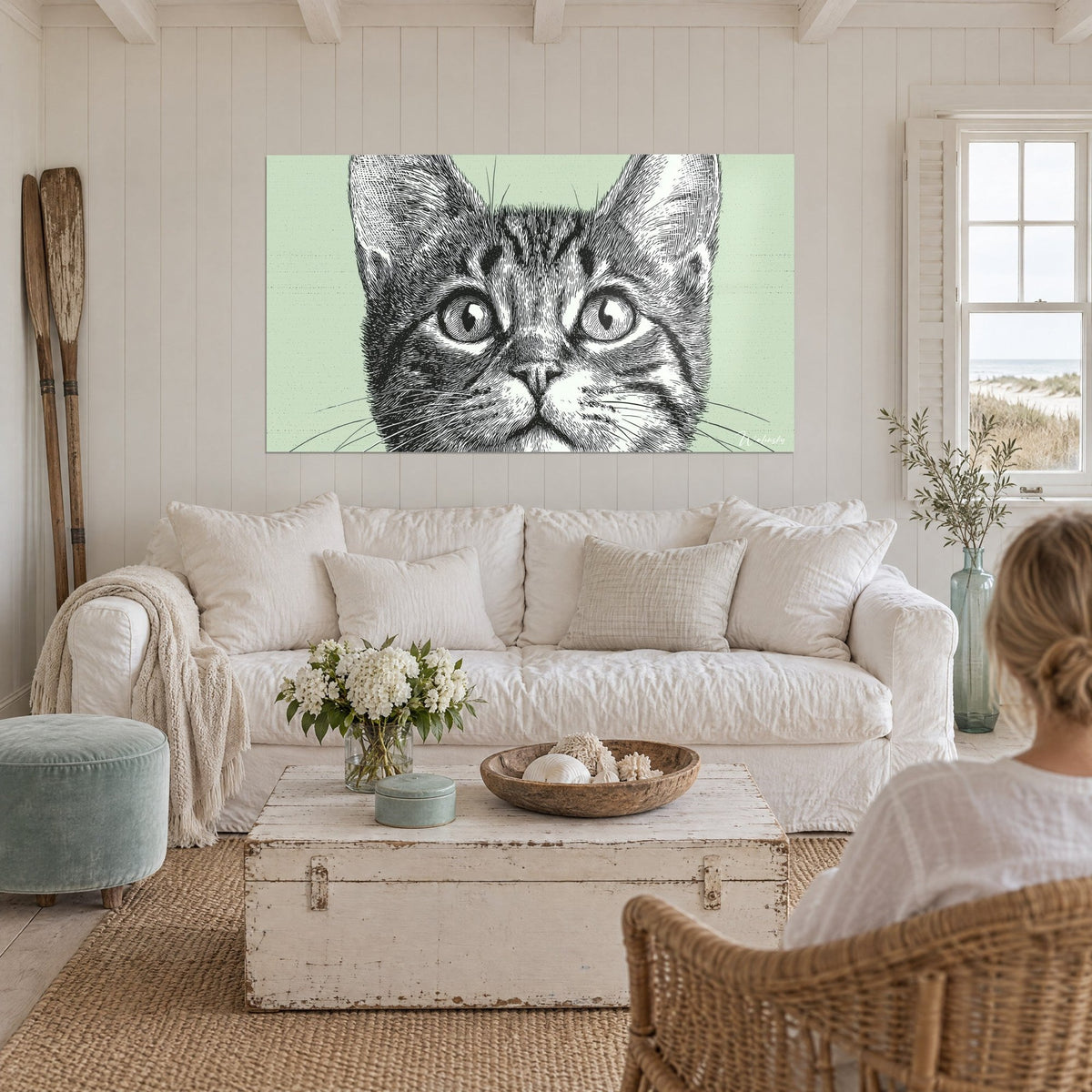 Gemälde Tigerkätzchen mit großen runden Augen, Schwarz-Weiß-Gravur auf salbeigrünem Hintergrund, über einem Sofa in einem hellen Wohnzimmer