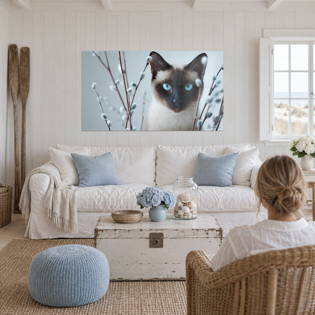Wall art Siamese cat with turquoise eyes among grey willow catkins, pale blue background, above a sofa in a bright living room