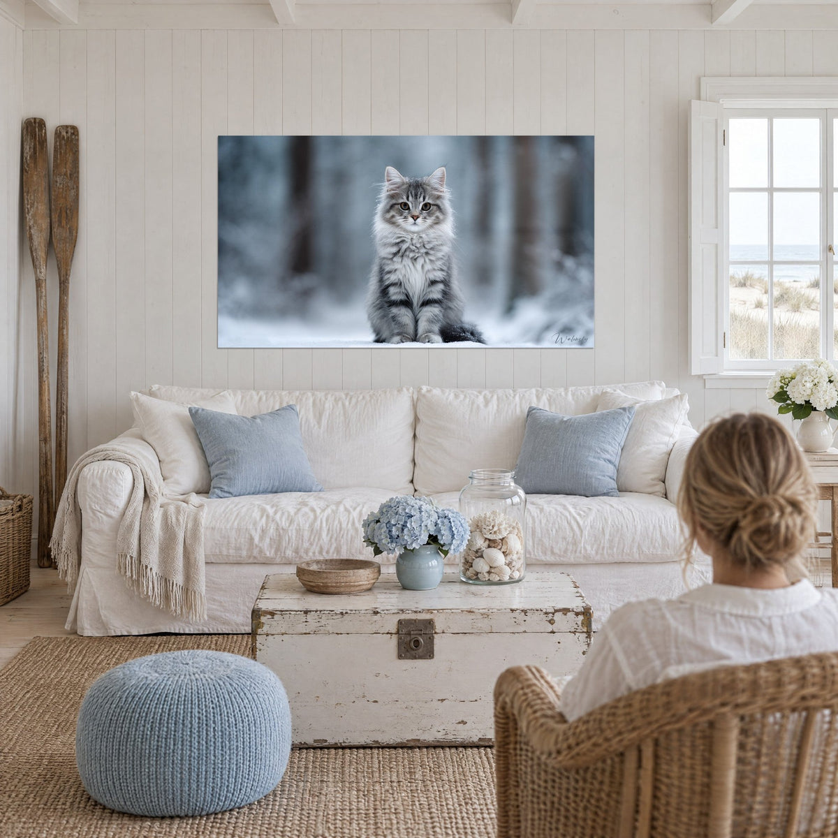 Wall art of a grey and white Siberian kitten sitting in the snow, amber eyes, blurred blue-tinted forest, hanging above a sofa in a bright living room