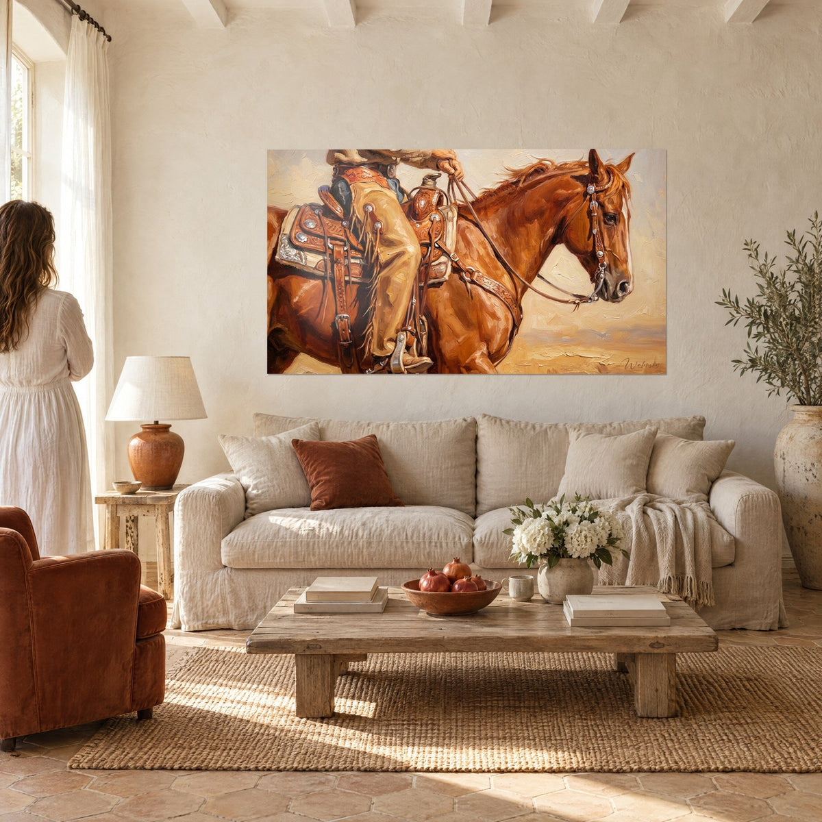 Tableau cowboy en chaps beiges tenant les rênes d'un alezan, selle cuivrée ornée d'argent, au-dessus d'un canapé dans un salon lumineux