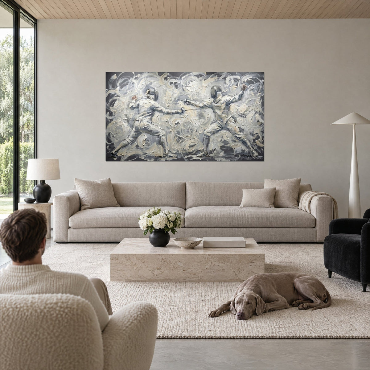 Wall art fencing duel in swirls of silver and cream white, two people seen from behind, grey dog, above a sofa in a bright living room