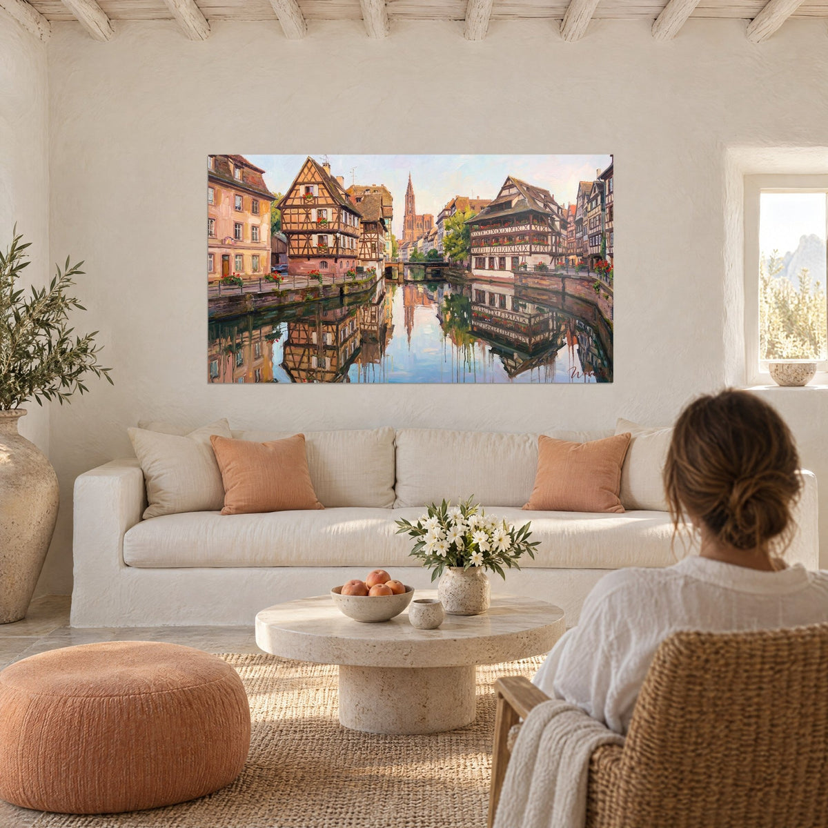 Gemälde Fachwerkhäuser im Elsass in Rost und Creme, rosa Turmspitze der Kathedrale, über einem Sofa in einem hellen Wohnzimmer