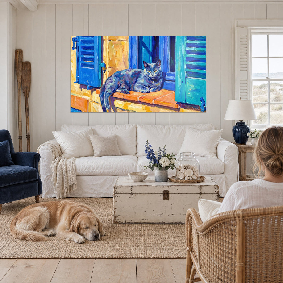 Tableau chat chartreux gris-bleu allongé sur un rebord de brique orangé, volets bleu roi, au-dessus d'un canapé dans un salon lumineux