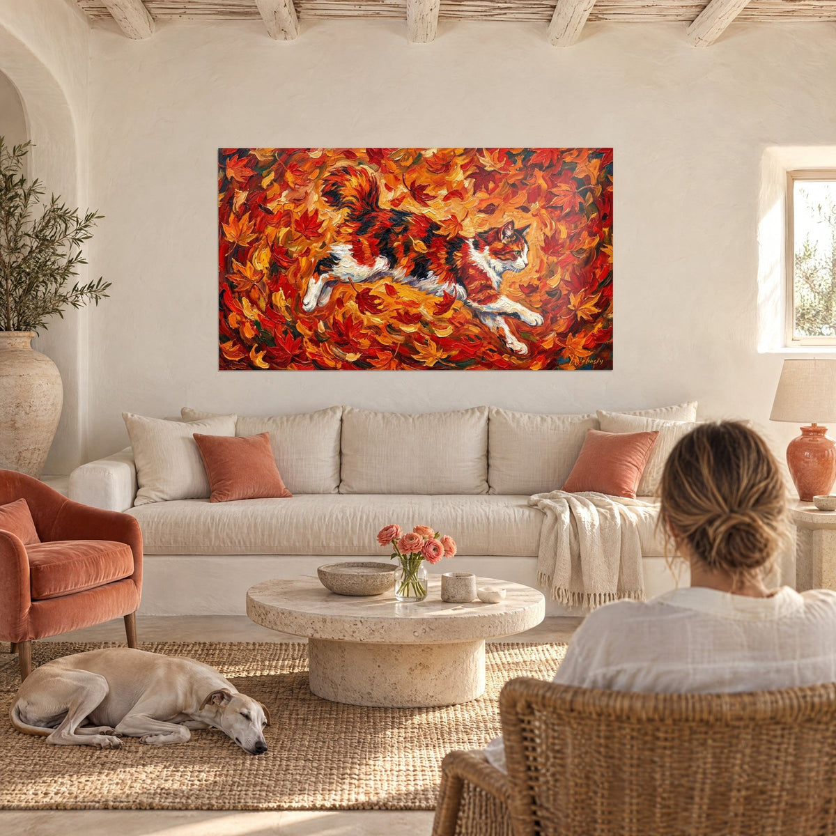 Quadro di un gatto tricolore che balza tra foglie rosse e arancioni, sopra un divano in un soggiorno luminoso