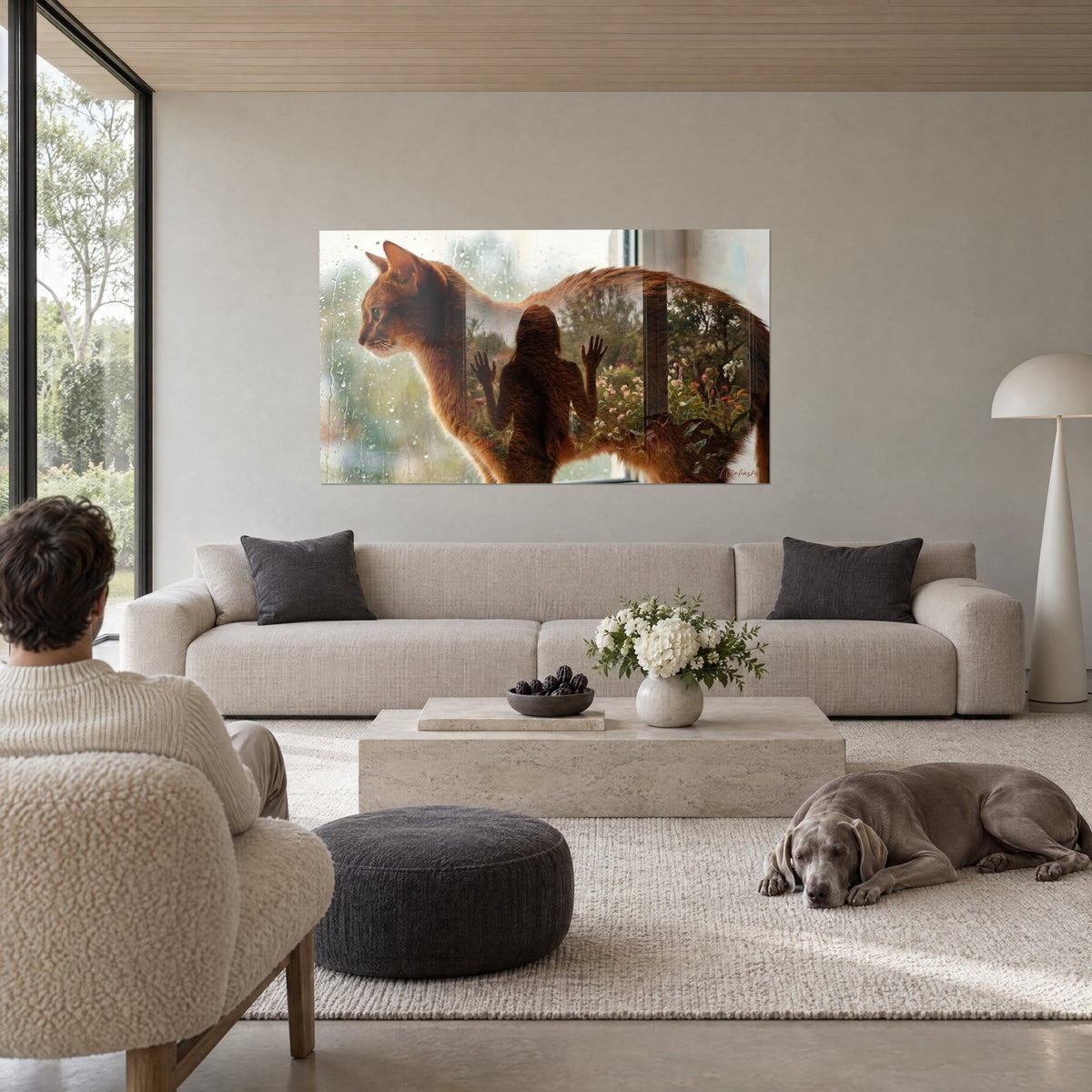 Gemälde Abessinierkatze kupferfarben in Doppelbelichtung, Frauensilhouette und blühender Garten, über einem Sofa in einem hellen Wohnzimmer