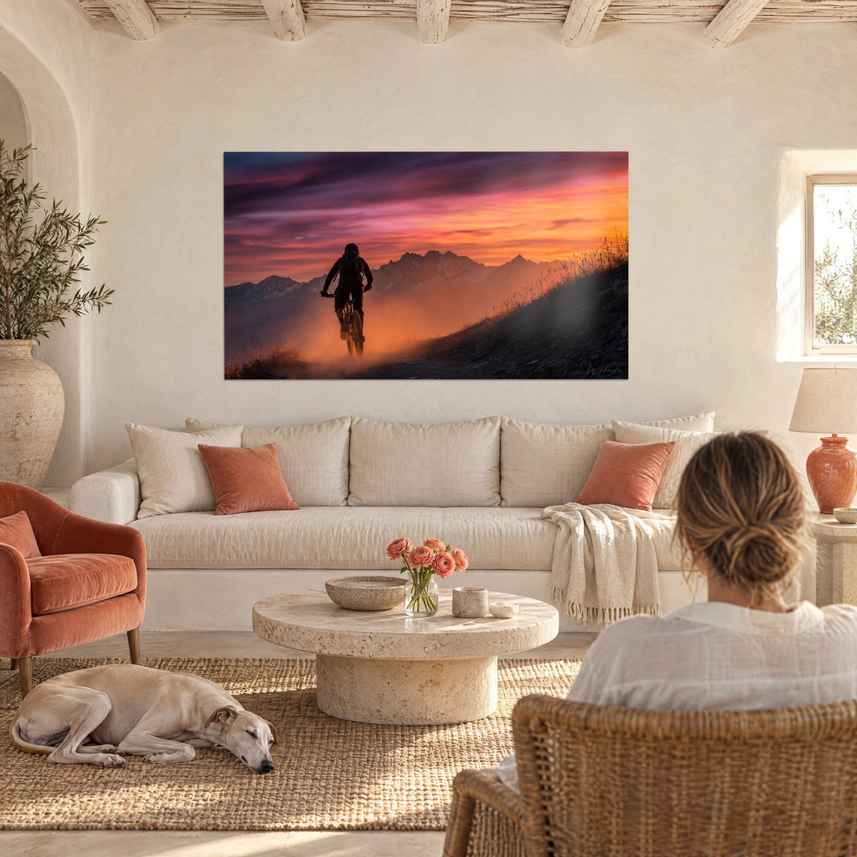 Gemälde eines Mountainbikers von hinten, der durch orangefarbenen Staub fährt, rosa und violetter Himmel, Alpengrate, über einem Sofa in einem hellen Wohnzimmer