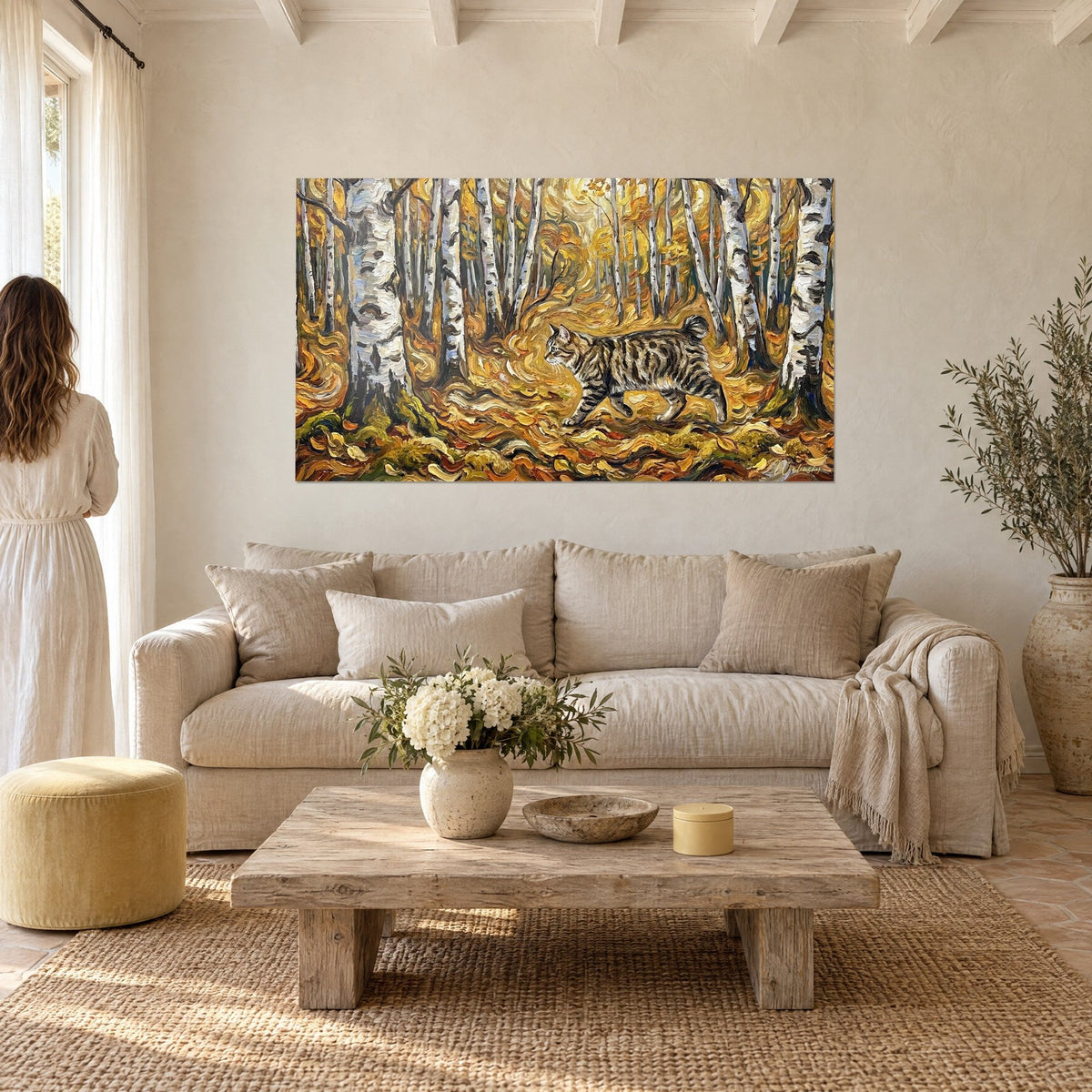 Tableau chat tigré cheminant entre des bouleaux argentés, feuilles ocre et dorées, au-dessus d'un canapé dans un salon lumineux