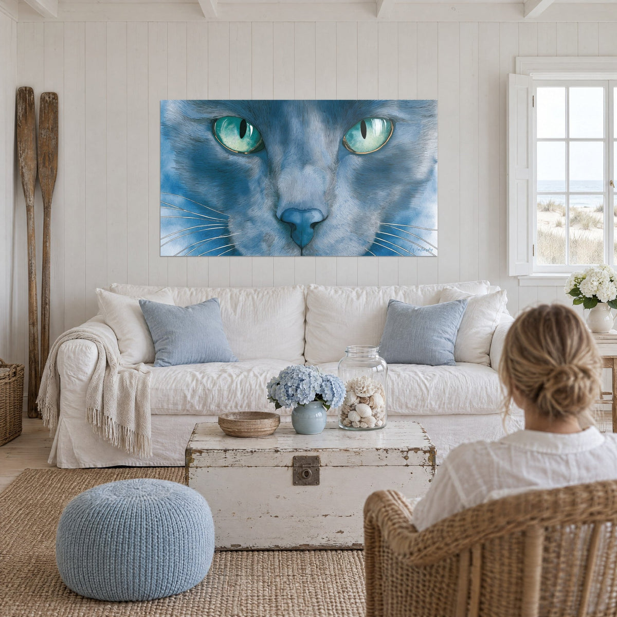 Tableau chat bleu-gris aux yeux turquoise, regard fixe et moustaches blanches, au-dessus d'un canapé dans un salon lumineux