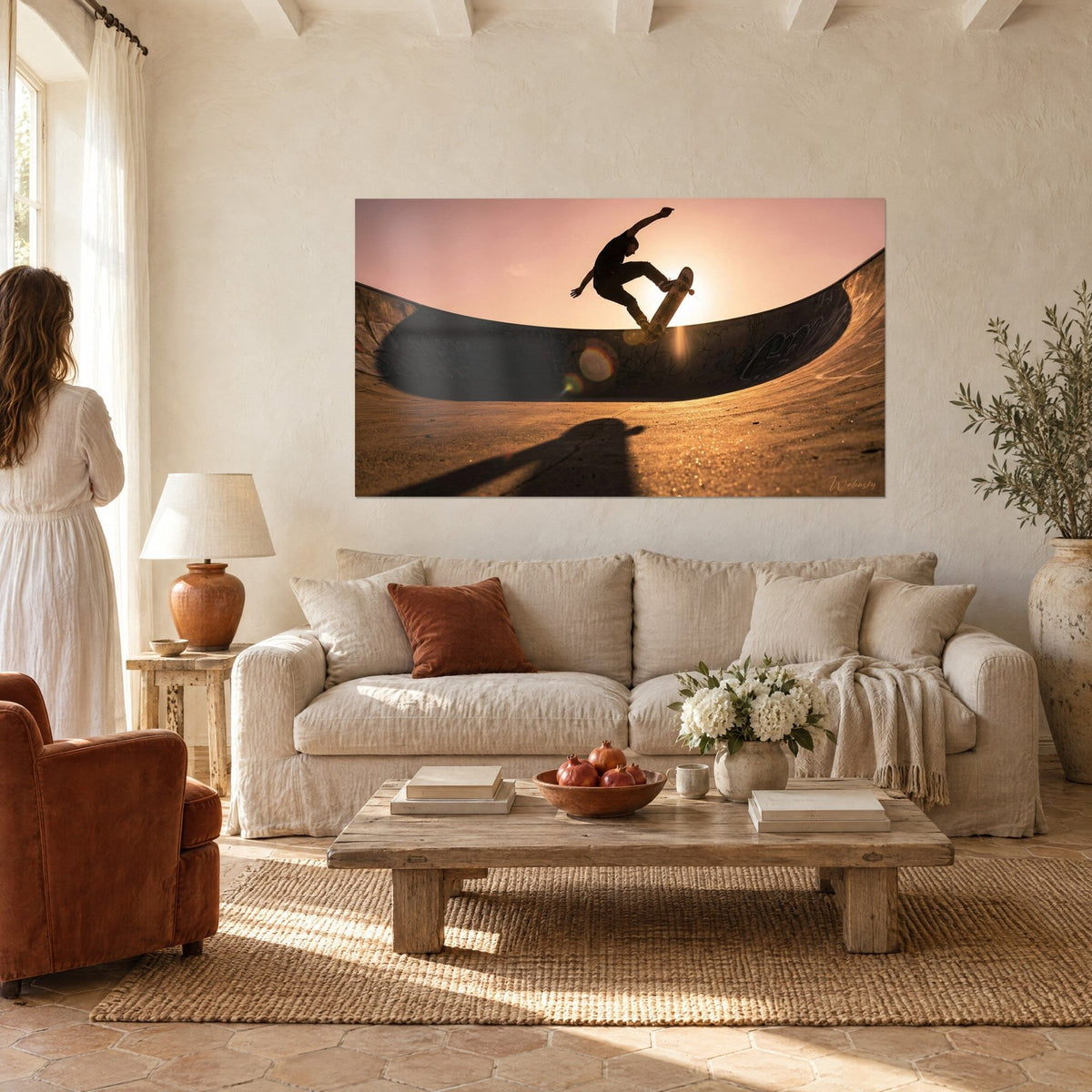 Quadro di uno skater in pieno salto stagliato in silhouette davanti a un sole rosa e arancio dentro un bowl grigio, sopra un divano in un soggiorno luminoso