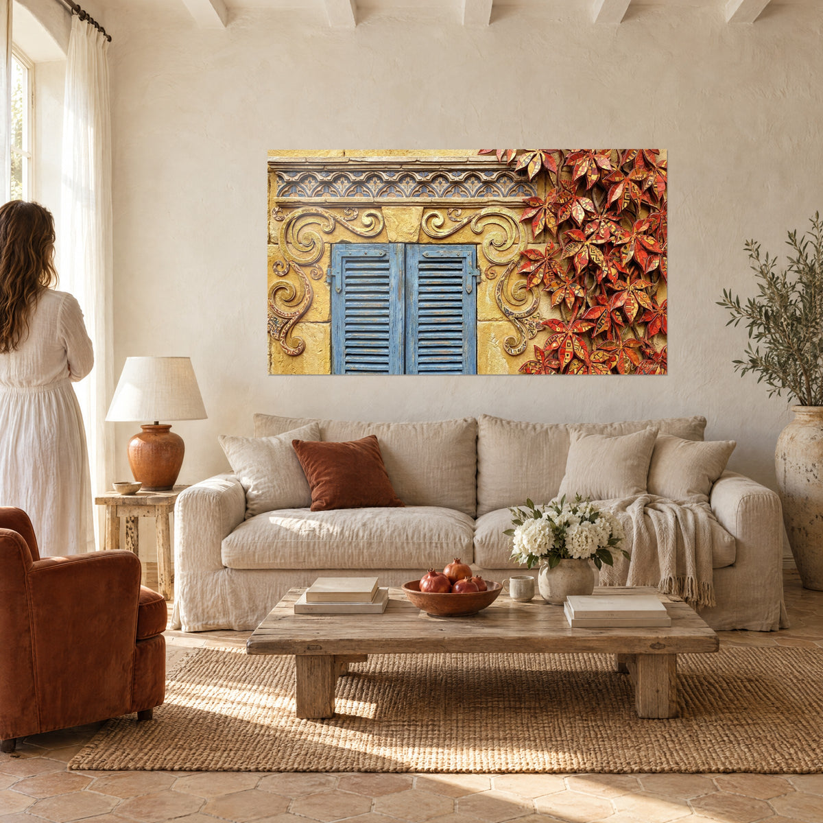 Quadro facciata provenzale con persiane azzurre sbiadite, foglie di vite rosse e ocra, donna di spalle sopra un divano in un soggiorno luminoso