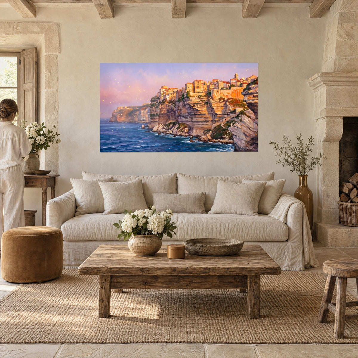 Cuadro ciudadela de Bonifacio dorada sobre acantilados calizos, mar azul cobalto, cielo rosa, persona de espaldas, encima de un sofá en un salón luminoso