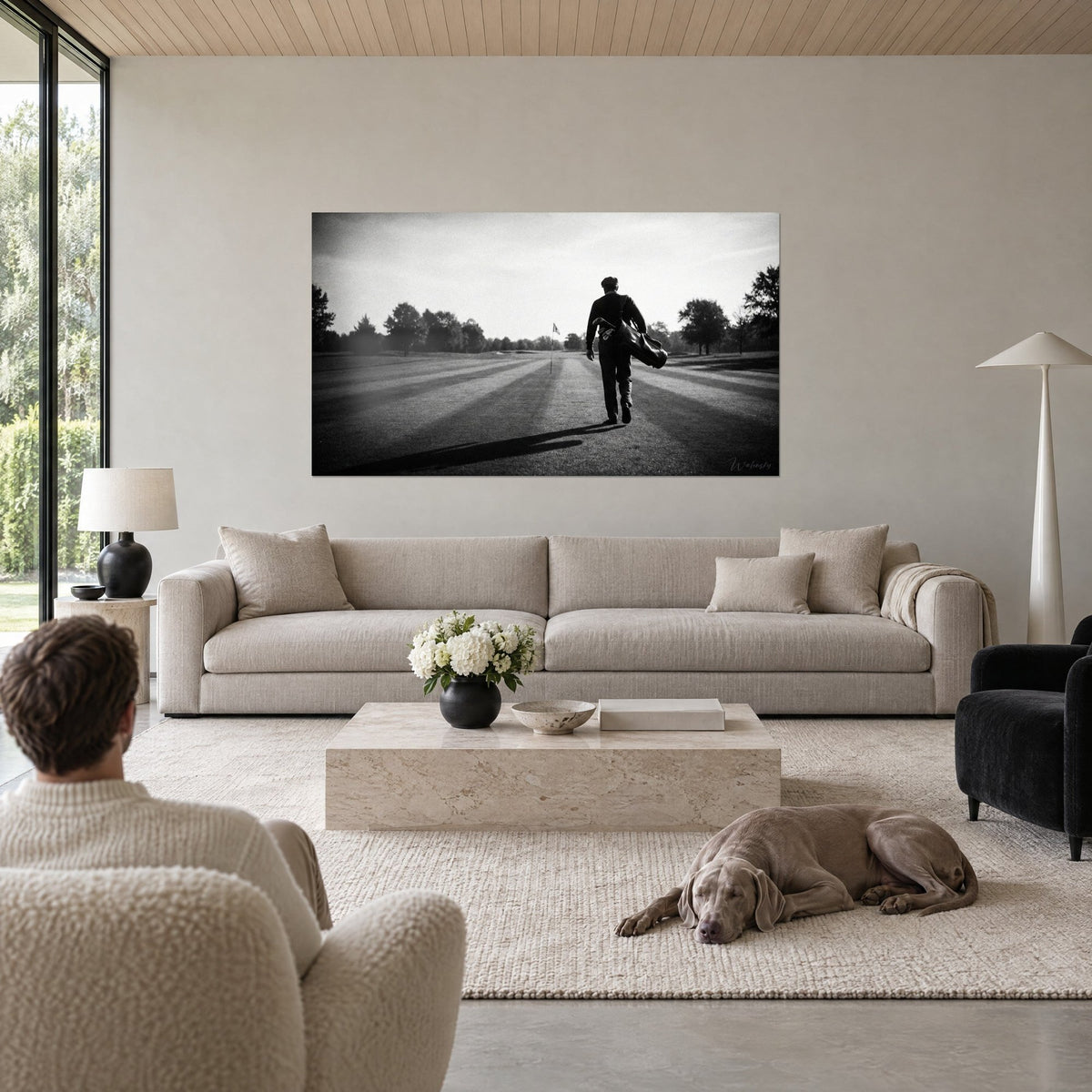 Schilderij van een eenzame golfer in zwart-wit, golftas over de schouder, zilvergrijs en diepzwart, boven een bank in een lichte woonkamer