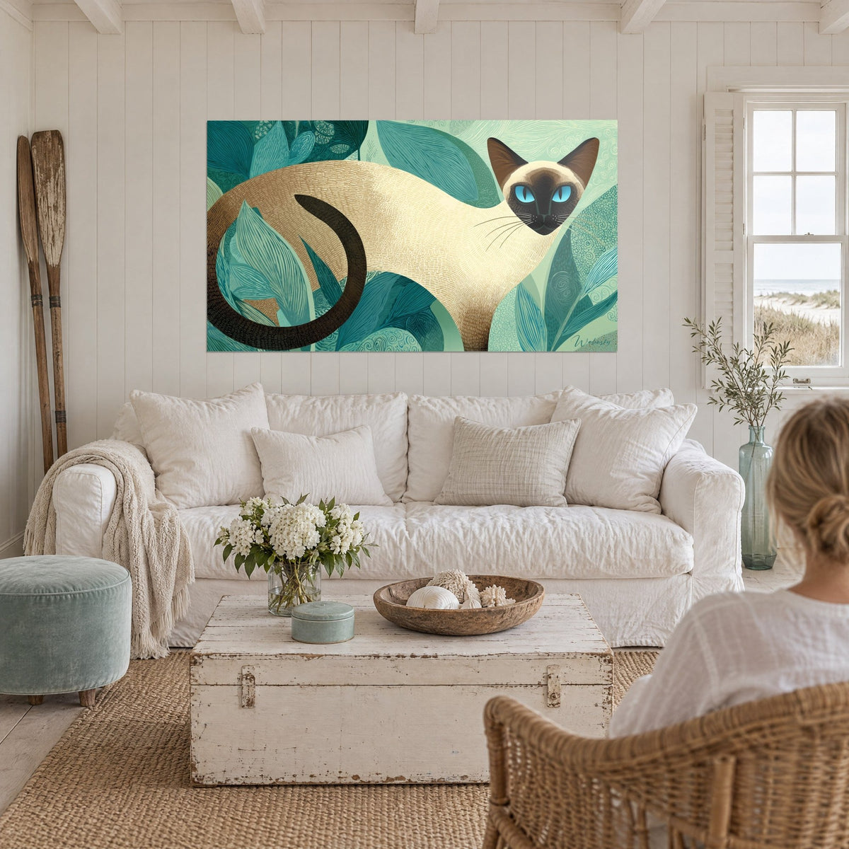 Quadro gatto siamese color crema con occhi turchesi tra foglie verde menta, sopra un divano in un soggiorno luminoso
