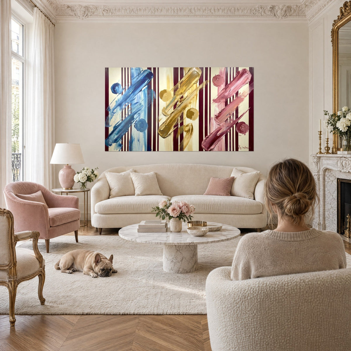 Wall art triptych of thick brushstrokes in blue, gold and pink on a cream background with burgundy stripes, above a sofa in a bright living room