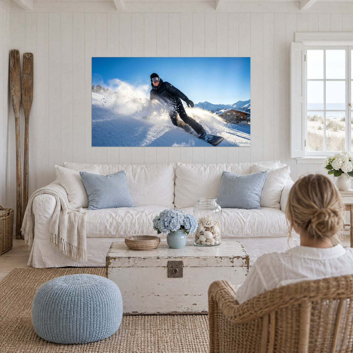 Gemälde Lächelnder Snowboarder, der eine Fontäne weißen Pulverschnees unter blauem Himmel aufwirbelt, über einem Sofa in einem hellen Wohnzimmer