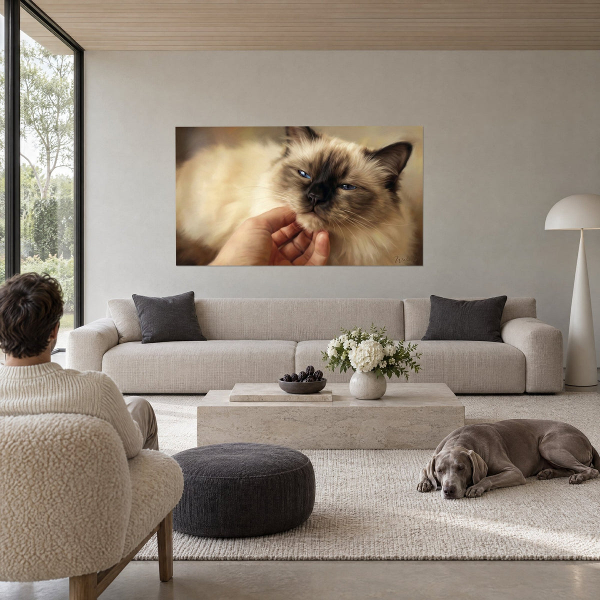 Schilderij Birmaanse kat met crèmekleurige vacht en bruin masker, een hand die over haar kin strijkt, boven een bank in een lichte woonkamer