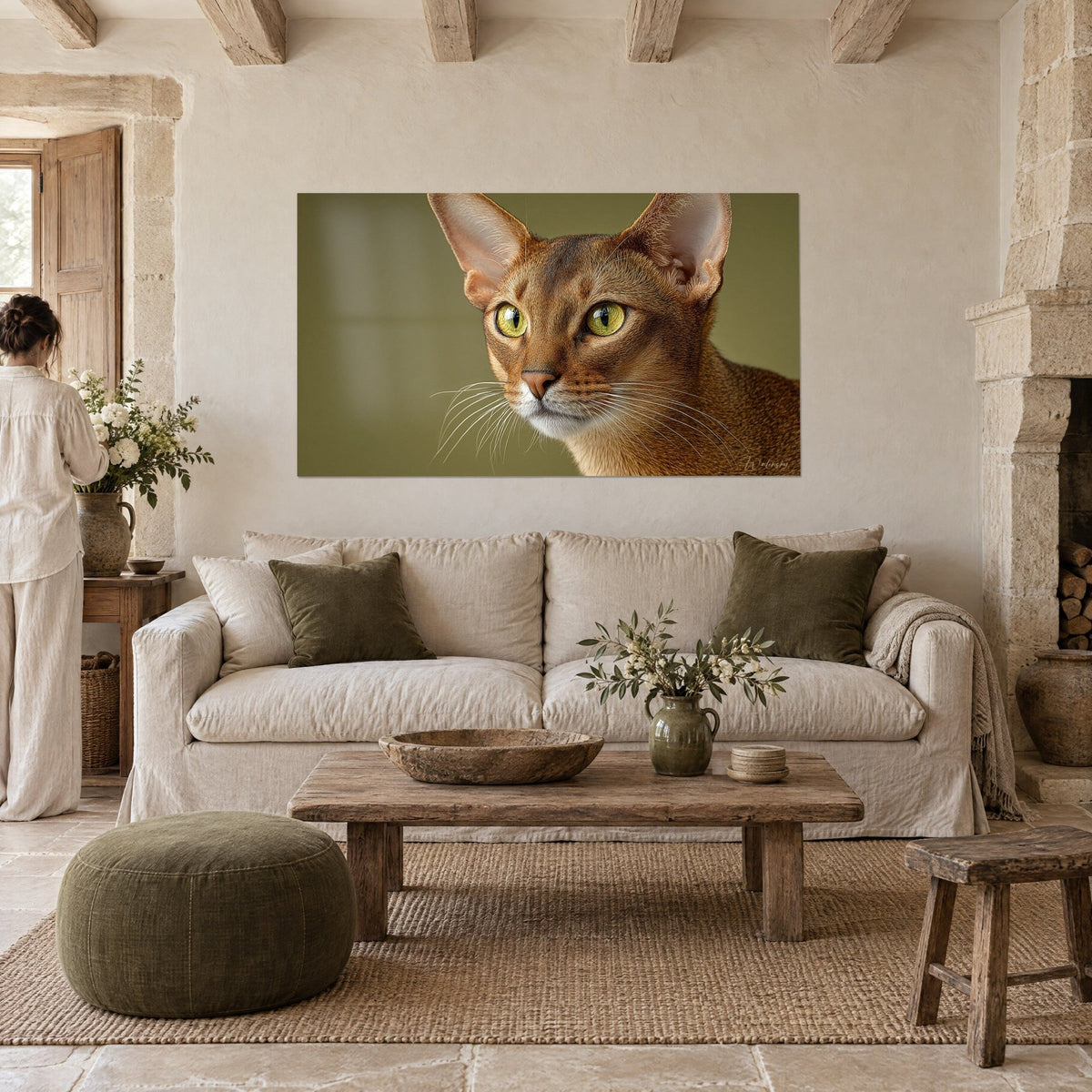 Tableau chat chausie aux yeux dorés, pelage roux et fond vert olive, personne de dos, au-dessus d'un canapé dans un salon lumineux