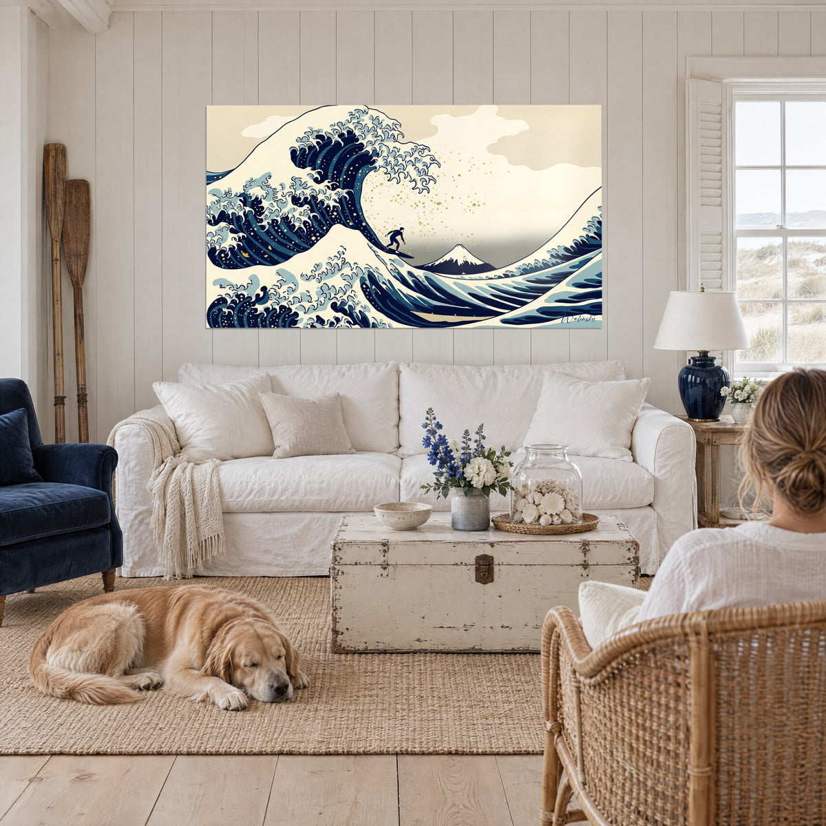 Cuadro ola japonesa rompiendo en azul medianoche y crema, diminuto surfista bajo la cresta, dos personas de espaldas y un retriever, encima de un sofá en un salón luminoso