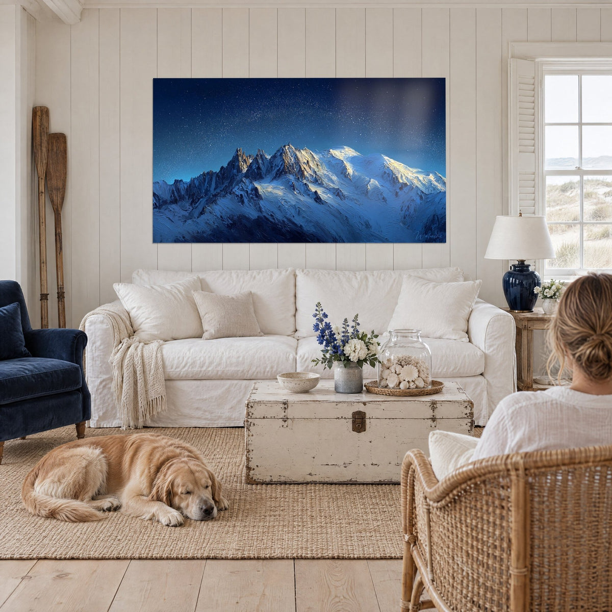 Cuadro macizo montaña nevada bajo la Vía Láctea, crestas azul noche y doradas, perro retriever tumbado, encima de un sofá en un salón luminoso