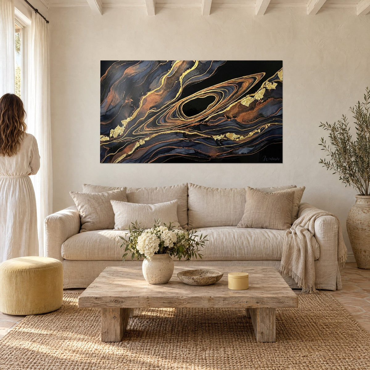 Tableau vortex ovale cerclé d'or sur fond noir et bleu nuit, feuilles d'or éclatées, femme de dos, au-dessus d'un canapé dans un salon lumineux