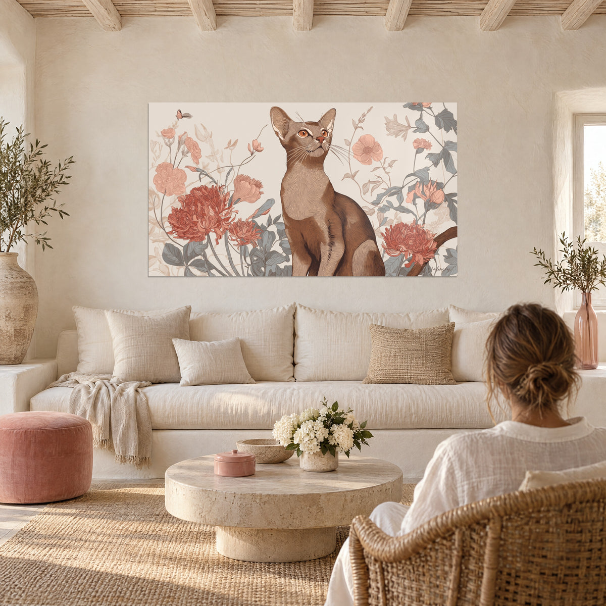 Gemälde einer rotbraunen Abessinierkatze, umgeben von korallenroten Pfingstrosen, betrachtet von einer Frau mit dem Rücken zum Betrachter über einem Sofa in einem hellen Wohnzimmer