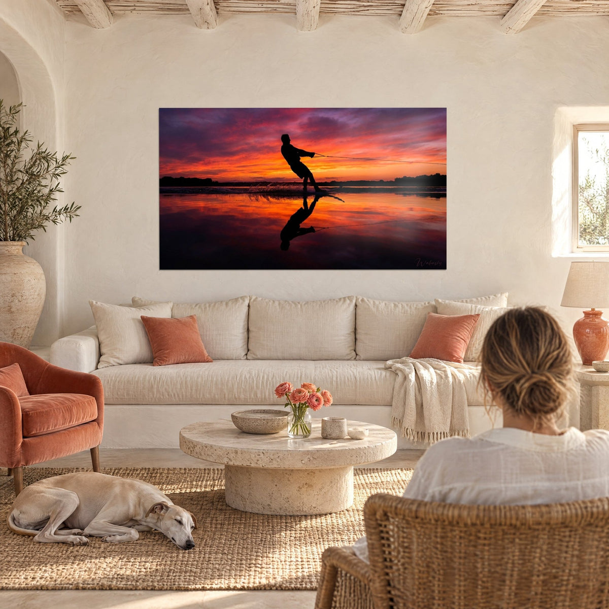 Gemälde Wasserskifahrer im Gegenlicht vor orangefarbenem und violettem Himmel, Spiegelung im Wasser, über einem Sofa in einem hellen Wohnzimmer