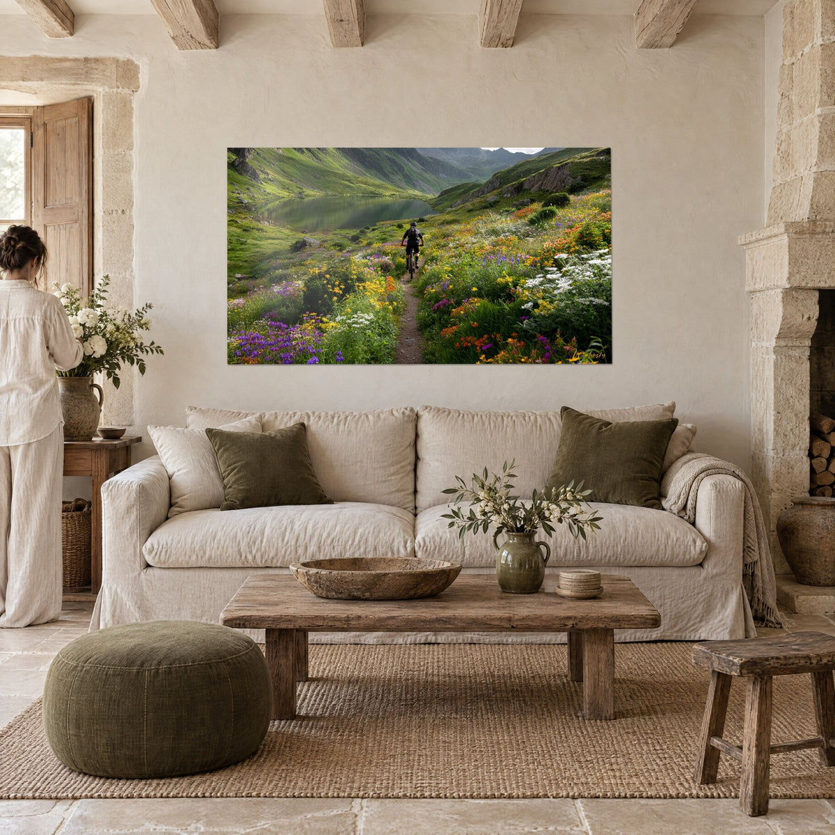 Wall art of a cyclist seen from behind on a flowery mountain trail, green lake and yellow, purple flowers, above a sofa in a bright living room