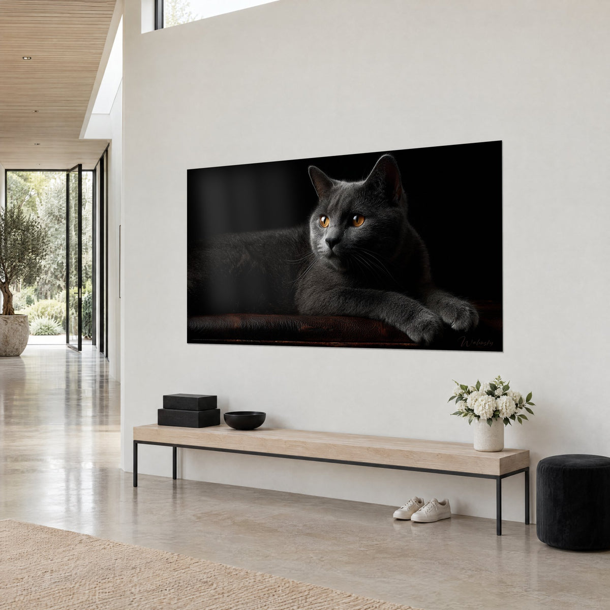 Wall art charcoal-grey feline with a golden gaze turned to the side, paw stretched over rust-coloured leather, black background, white wall in three-quarter view