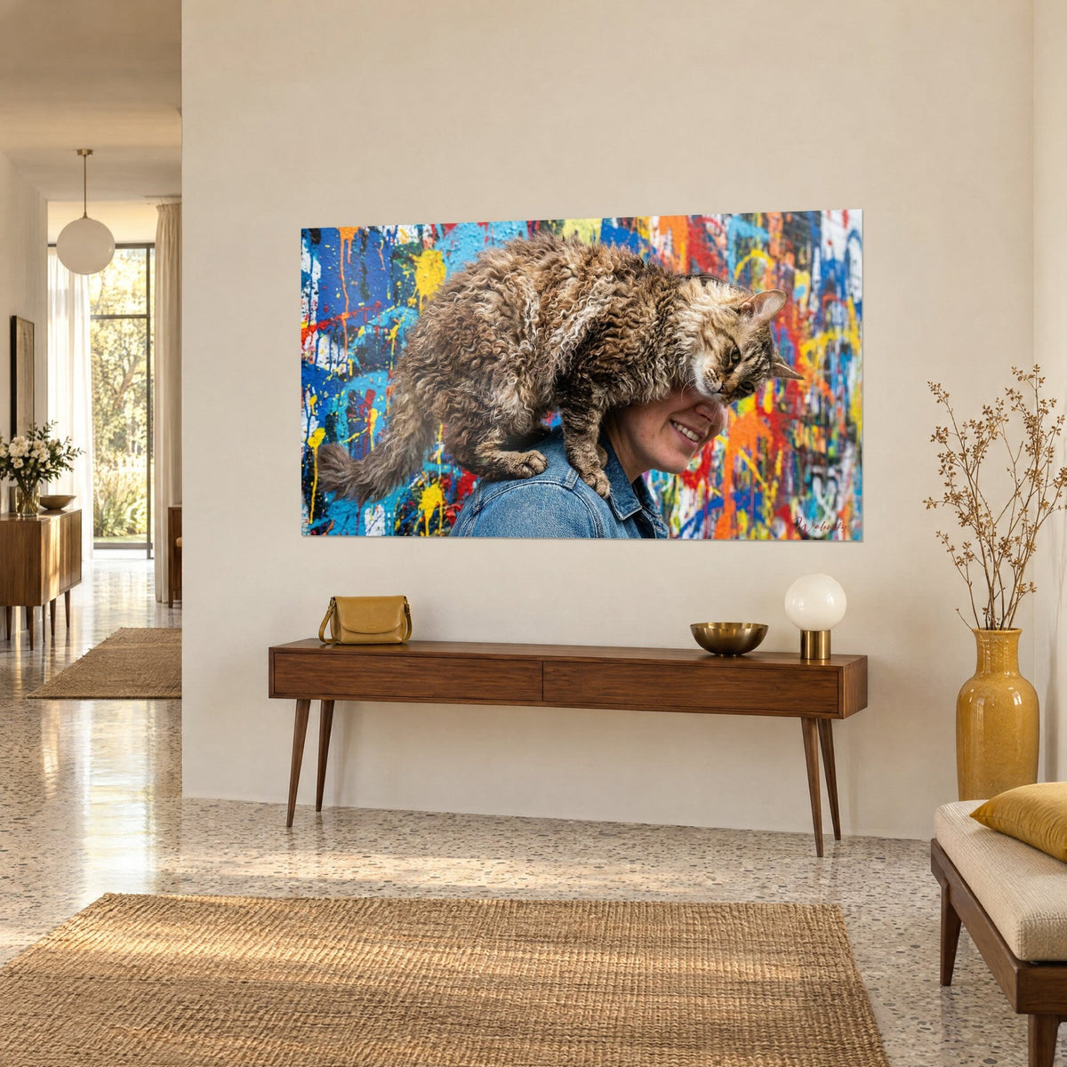 Quadro felino dal pelo arricciato disteso su una spalla di denim, schizzi gialli e rossi, vista a tre quarti su una consolle in legno scuro