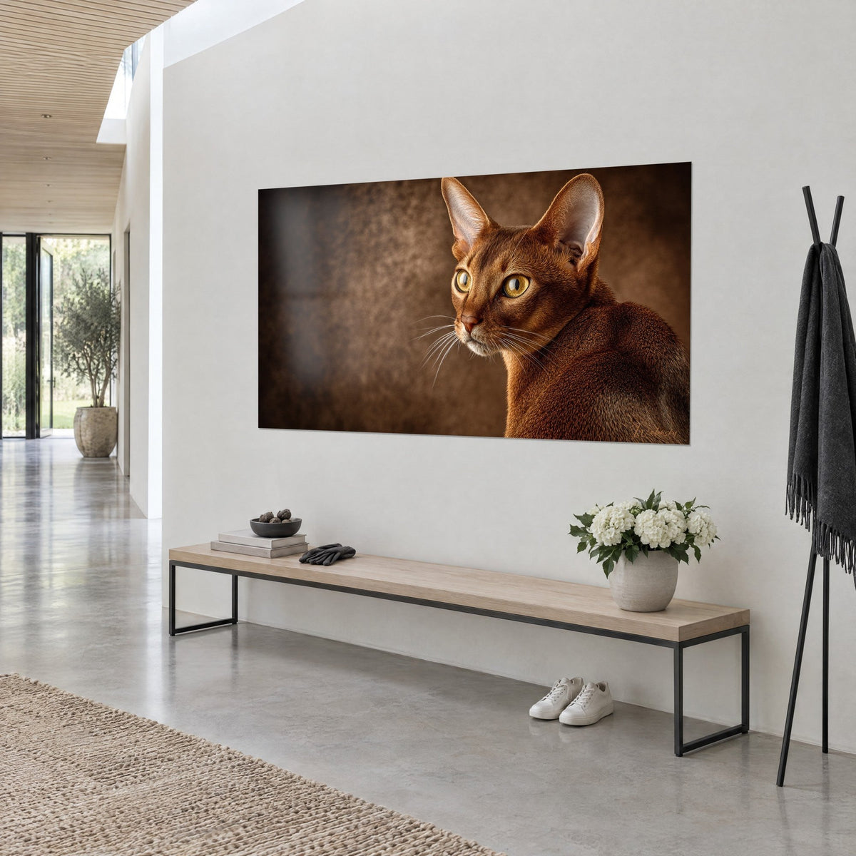 Cuadro felino cobrizo de perfil con finos bigotes blancos sobre fondo chocolate, pared clara de un recibidor luminoso en tres cuartos