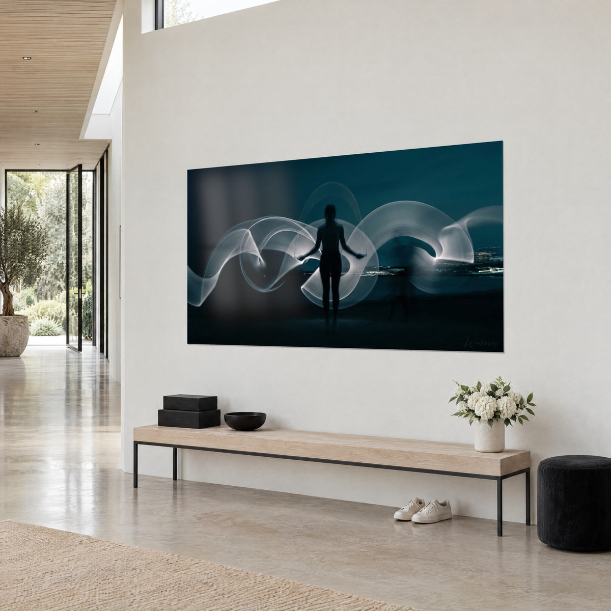 Tableau light painting d'une femme debout, volutes de lumière argentée sur un ciel bleu pétrole, accroché sur un mur beige clair