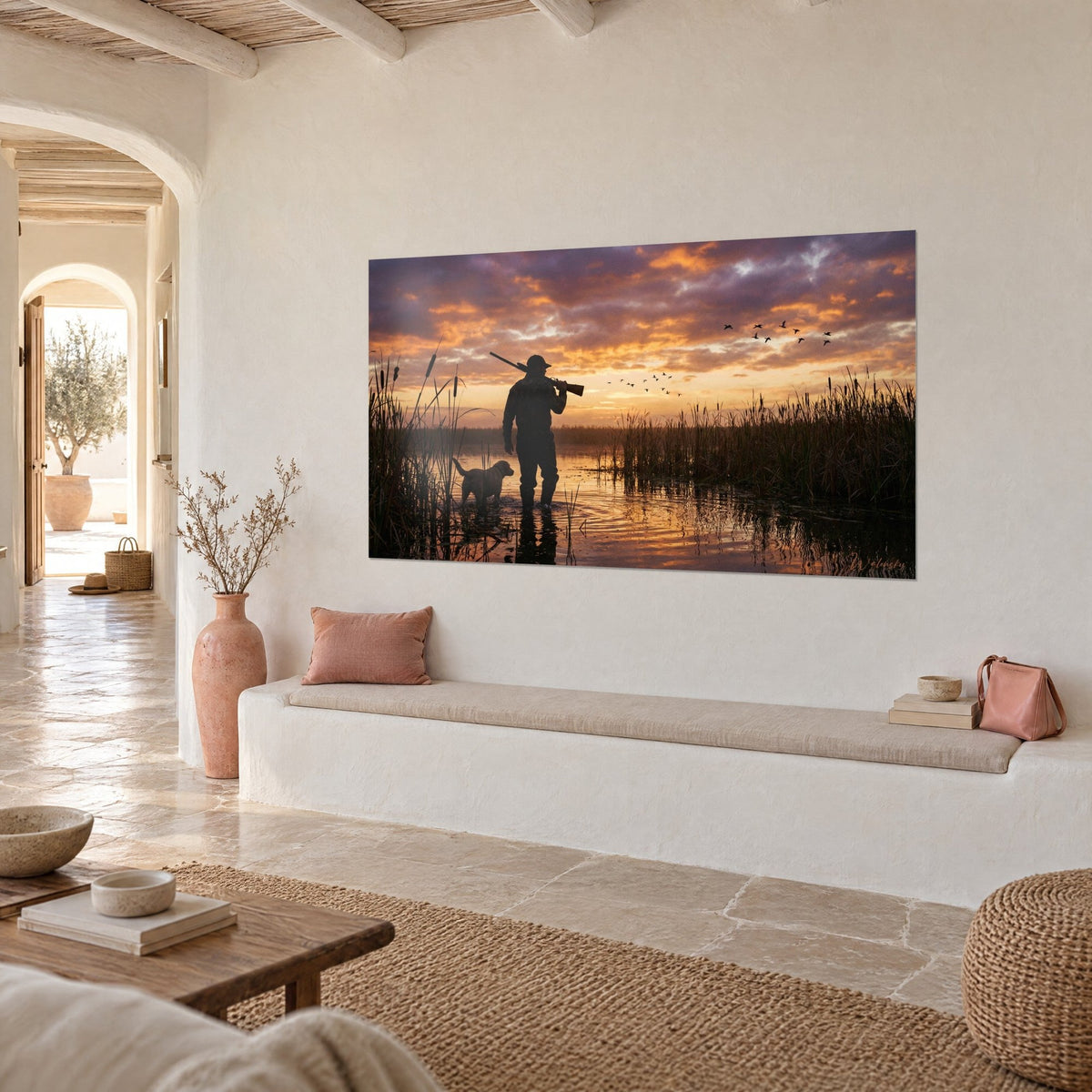 Quadro uomo in tuta mimetica e labrador color crema nell'acqua, riflessi dorati e canne scure, su una parete bianca d'ingresso