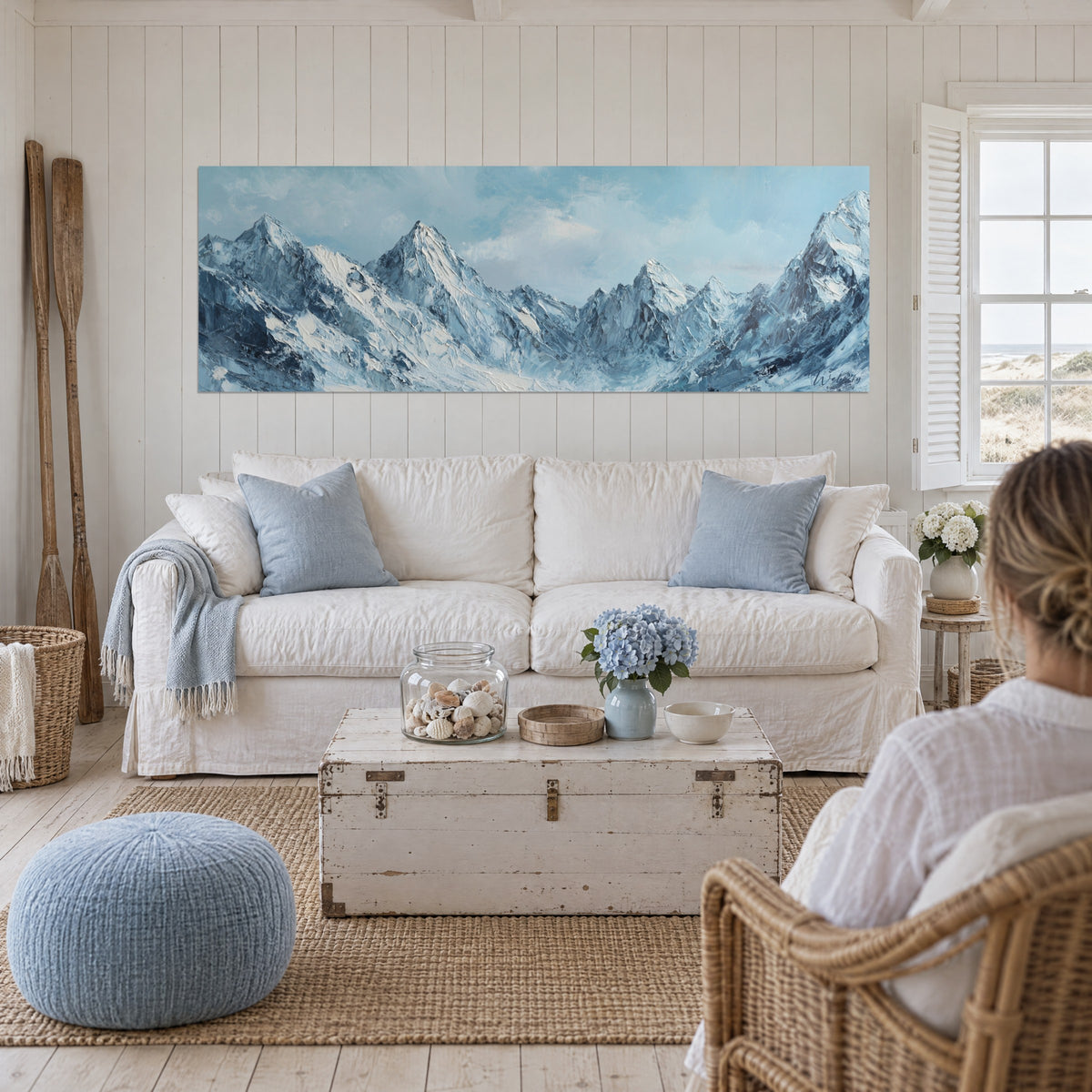 Cuadro cumbres alpinas nevadas en azul glaciar y blanco, cielo nublado, dos personas de espaldas encima de un sofá en un salón luminoso