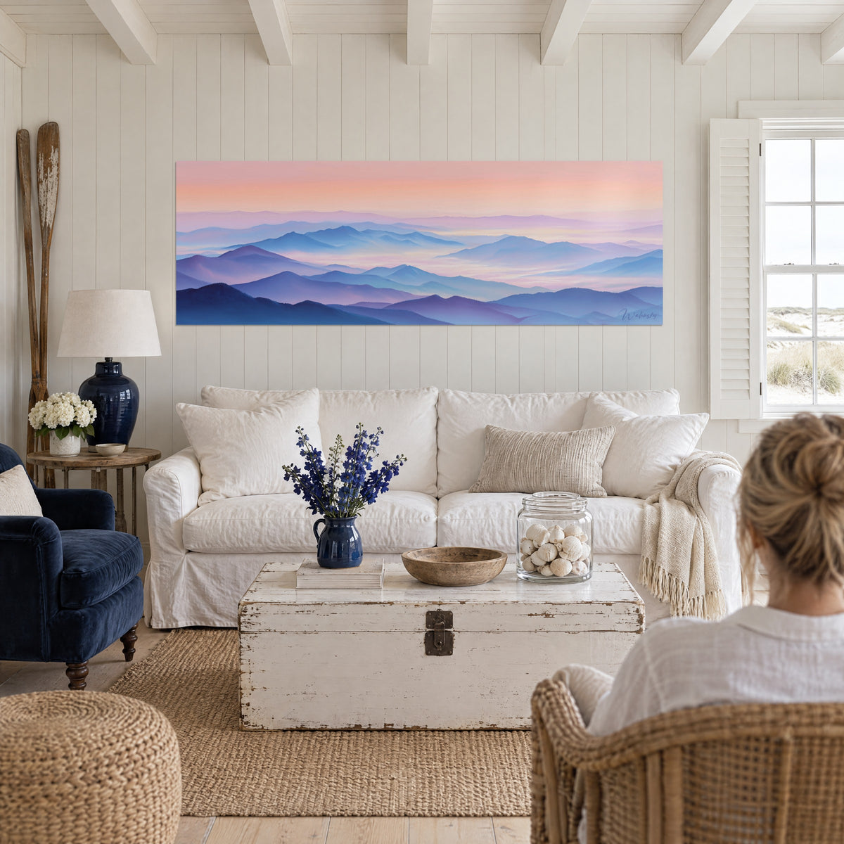 Wall art of bluish Pyrenean peaks under a salmon-pink sky, seen from behind, above a sofa in a bright living room