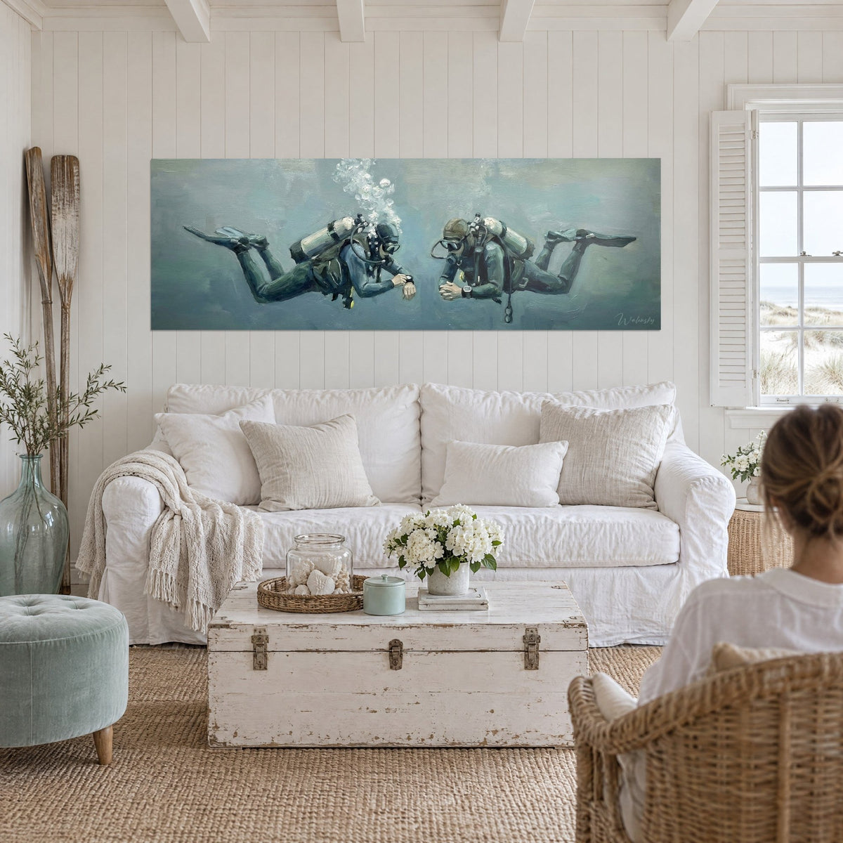 Wall art of two divers face to face in grey-blue water, silver bubbles, black fins, above a sofa in a bright living room