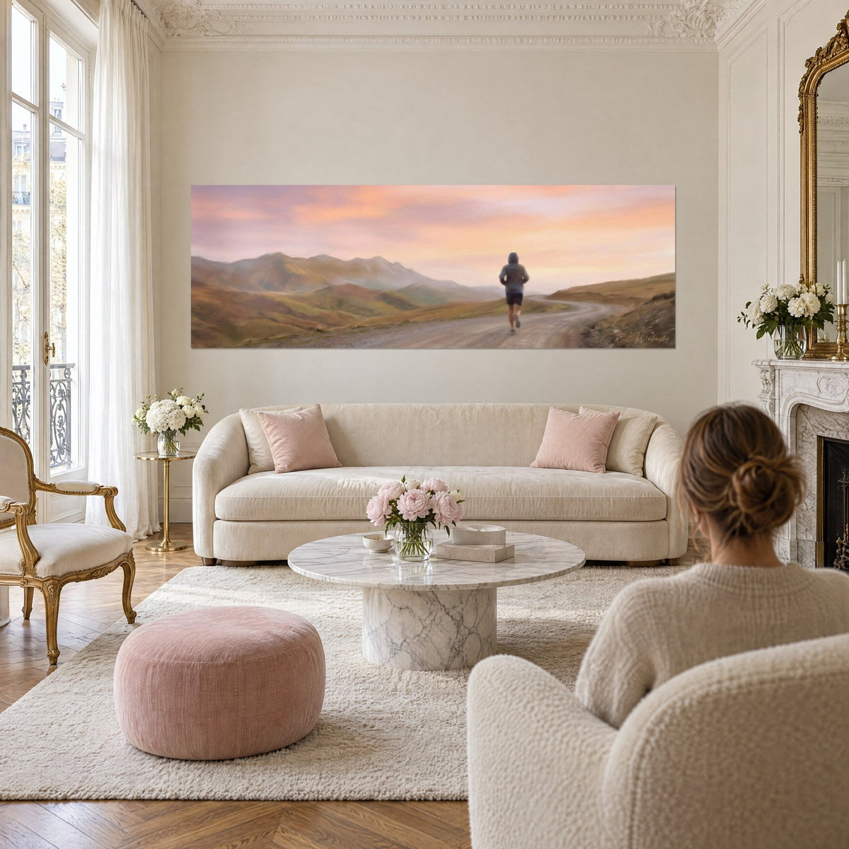 Wall art of a runner in a grey hood on a mountain trail, pink and orange sky, above a sofa in a bright living room