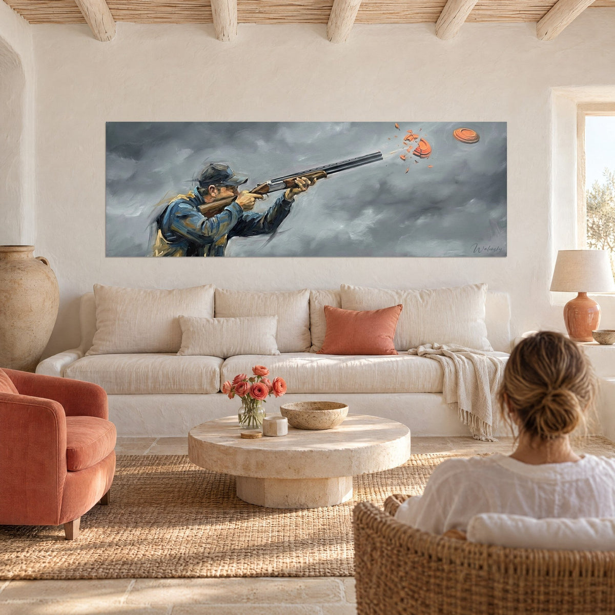 Wall art of a clay pigeon shooter with a shotgun, blue jacket against a stormy grey sky, above a sofa in a bright living room