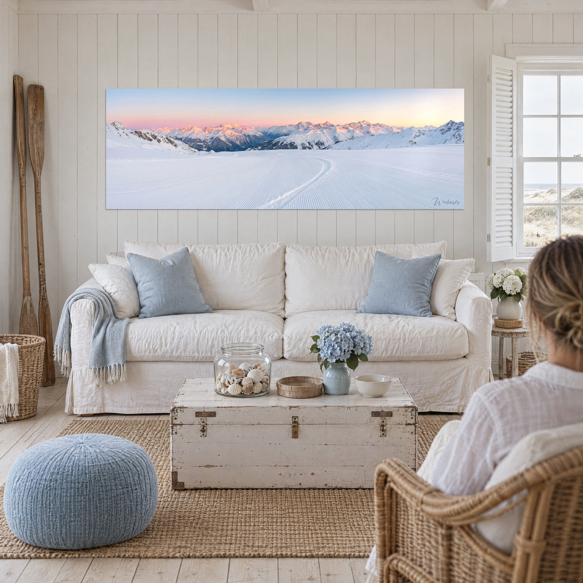 Wall art groomed ski slope at sunrise, pink peaks and bluish snow, above a sofa in a bright living room