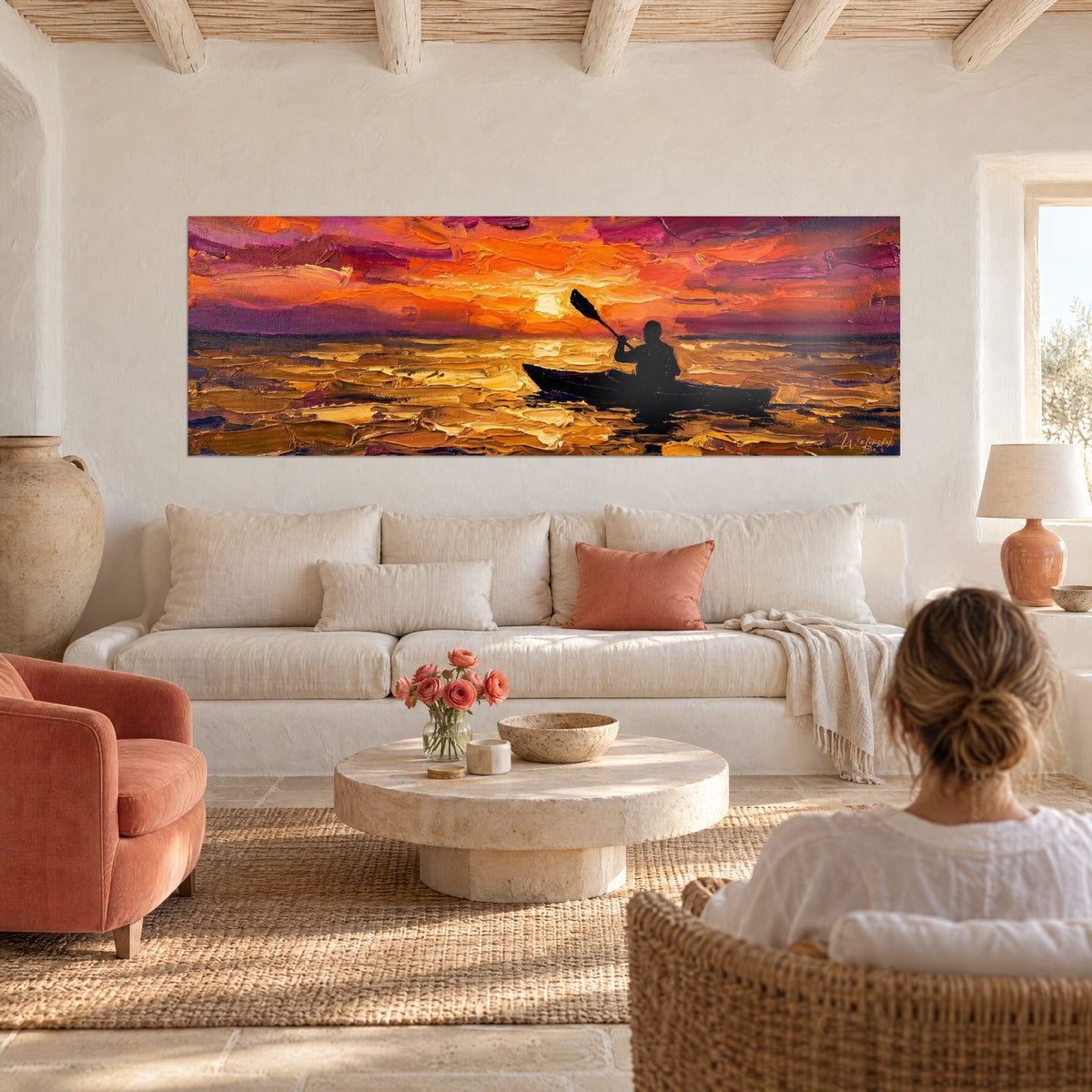 Wall art of a kayaker in silhouette paddling across a golden sea, orange and purple sky, above a sofa in a bright living room