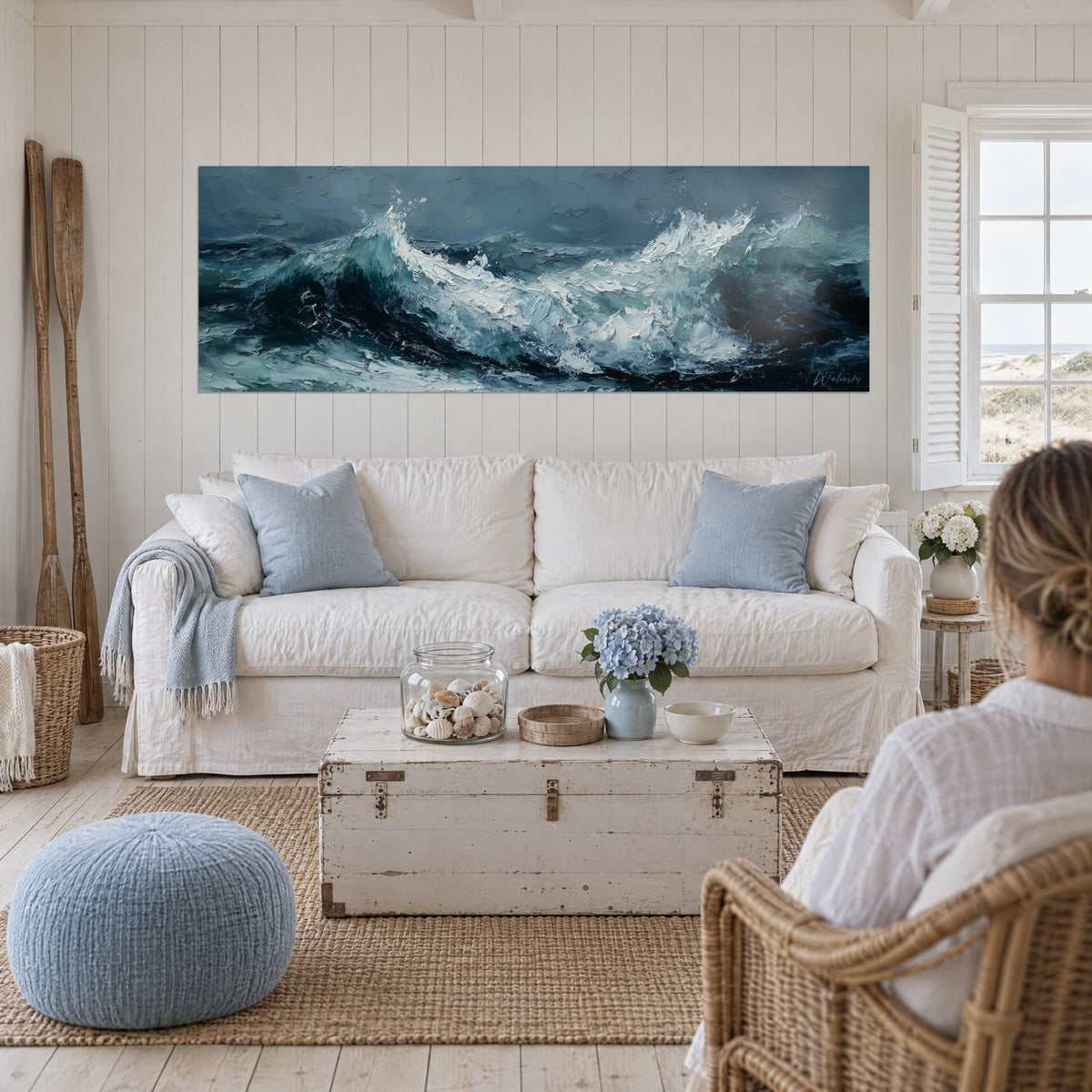 Gemälde stahlblaue Brandung mit dicken weißen Schaumkronen, zwei Personen von hinten, über einem Sofa in einem hellen Wohnzimmer