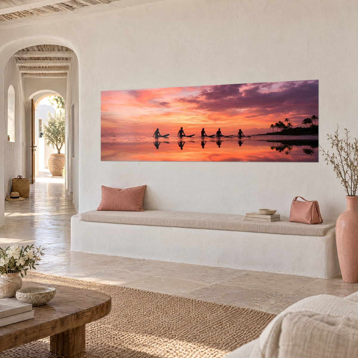 Cuadro siluetas de surfistas alineados sobre el océano rosa y púrpura, palmeras negras a la derecha, pared blanca de una casa mediterránea