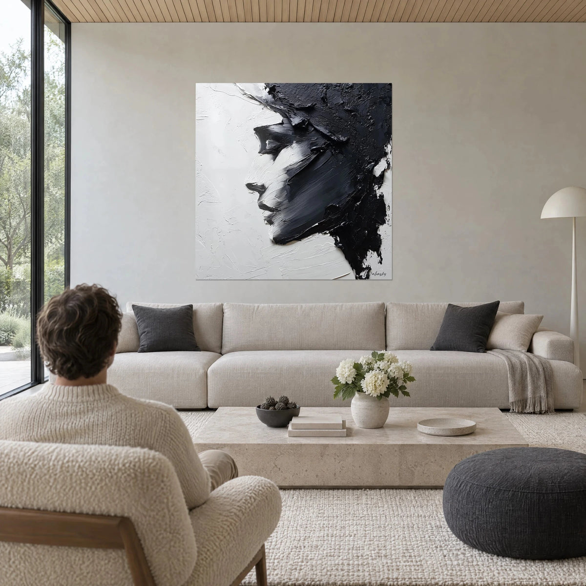 Tableau portrait expressionniste en profil, empâtements noirs sur fond blanc crème, au-dessus d'un canapé dans un salon lumineux