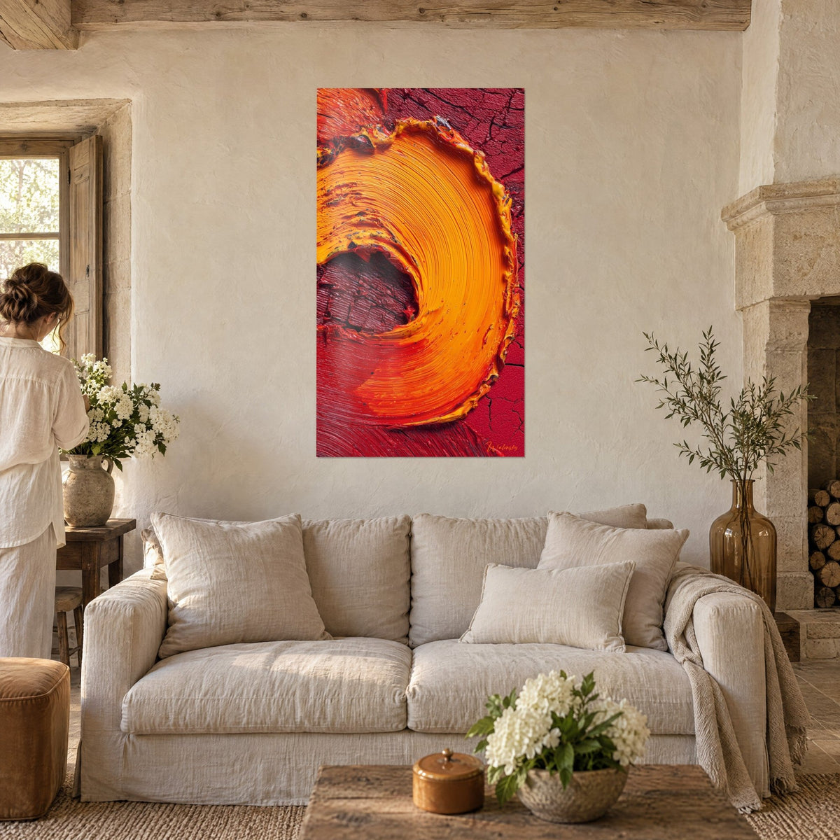 Wall art with a blazing orange spiral in thick impasto on a cracked red background, woman seen from behind, above a sofa in a bright living room