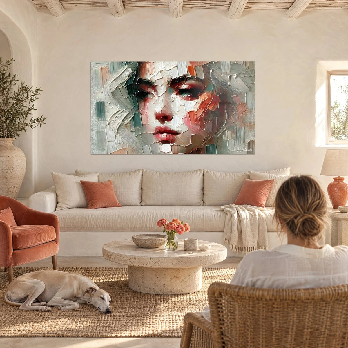 Wall art abstract portrait with grey and coral palette-knife strokes, woman's face, woman seen from behind and a greyhound, above a sofa in a bright living room