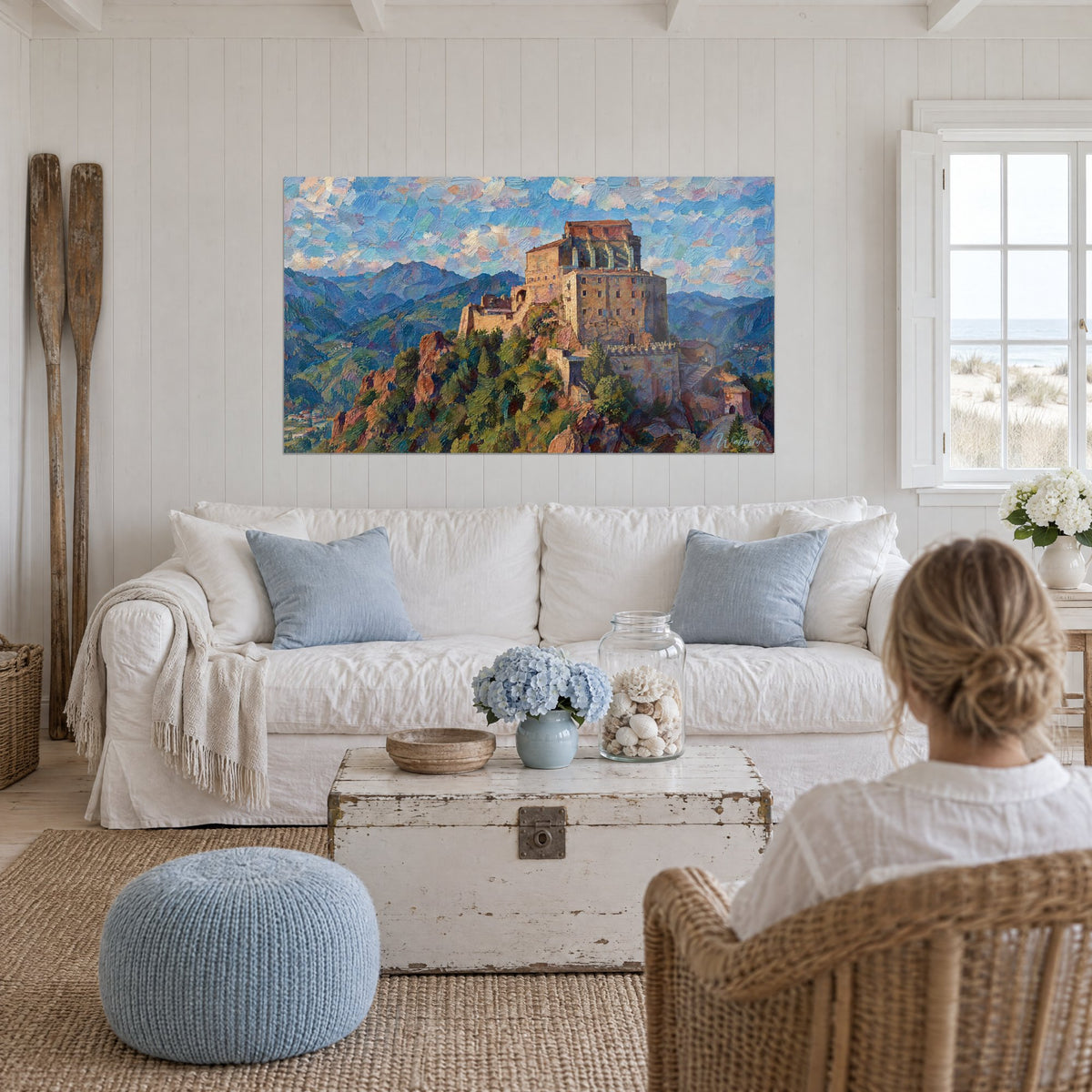 Gemälde einer Abtei aus ockerfarbenem Stein im Gleichgewicht auf einem Felssporn, blauer und rosa Himmel, über einem Sofa in einem hellen Wohnzimmer