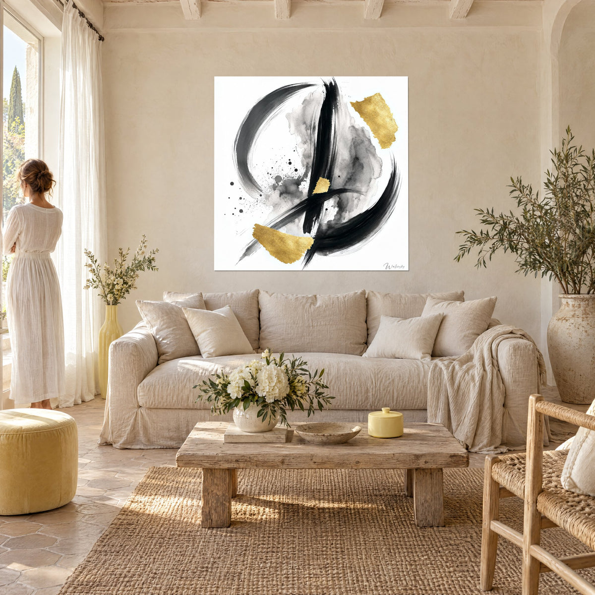 Schilderij met abstracte zwarte en gouden kalligrafie op een witte achtergrond, persoon van achteren, lichtbeige muren, boven een bank in een lichte woonkamer
