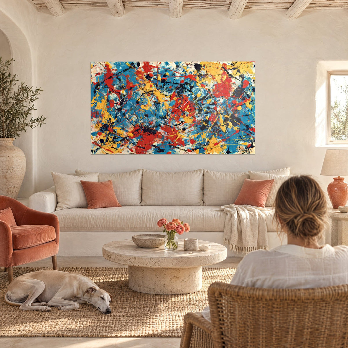 Tableau éclaboussures jaunes et rouges sur fond bleu, femme de dos et lévrier couché, au-dessus d'un canapé dans un salon lumineux